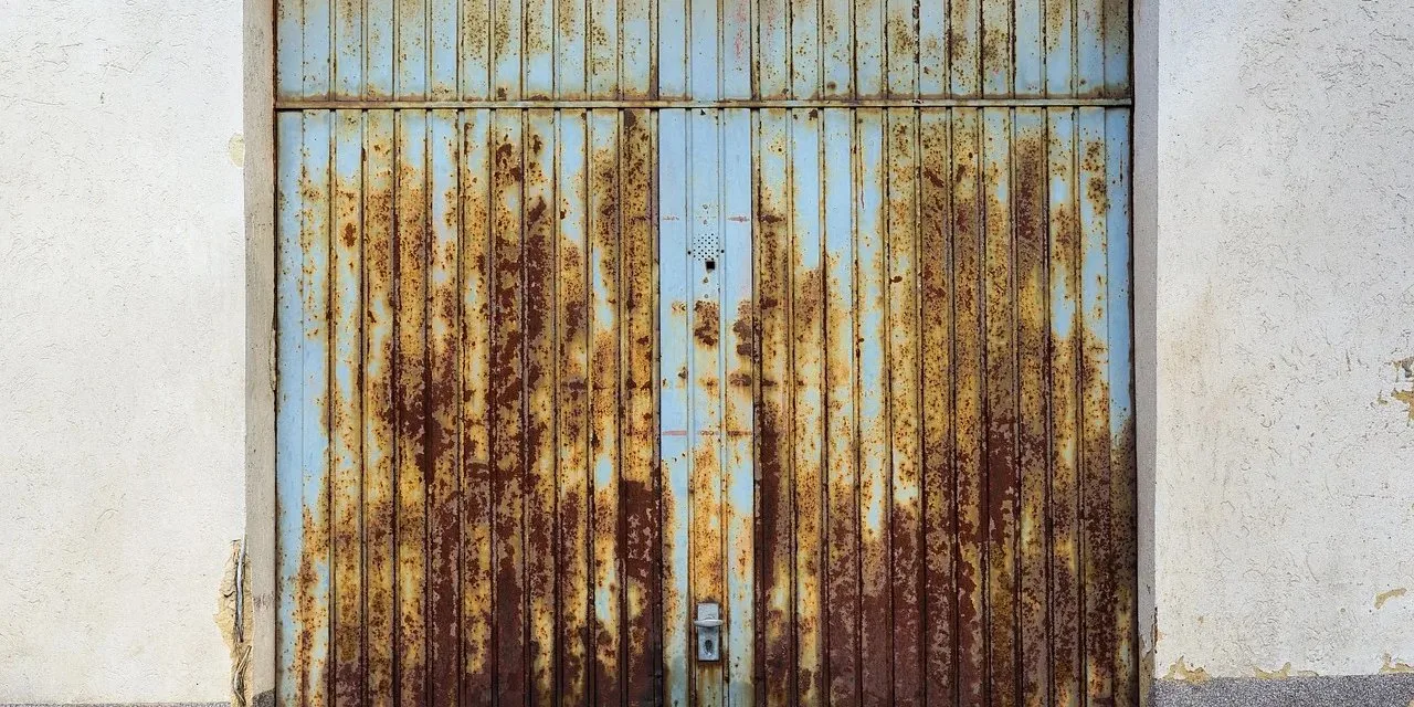 Garage Door Making Grinding Noise? 8 Causes, DIY Fixes & When to Call a Pro Rusty corroded garage door showing wear and age that causes grinding noise