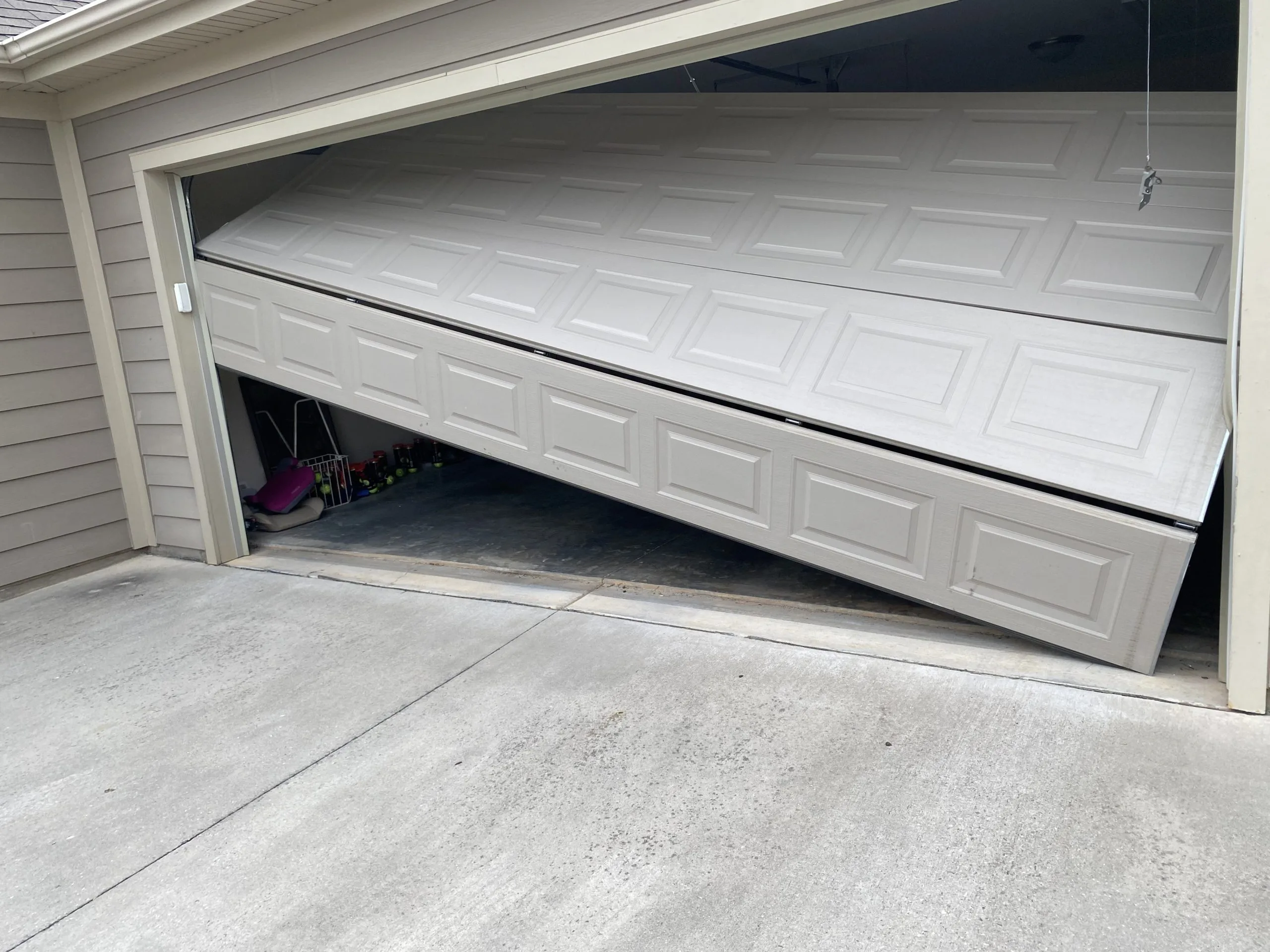 Garage Door Off Track? What to Do (And What Not to Do) Garage door off track and jammed at an angle with panels buckling outward from the opening