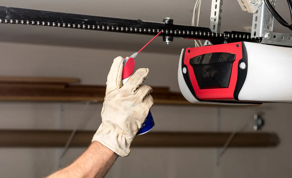 The Complete Garage Door Maintenance Schedule for Utah Homeowners Technician in work gloves lubricating a garage door opener chain rail during a maintenance service call
